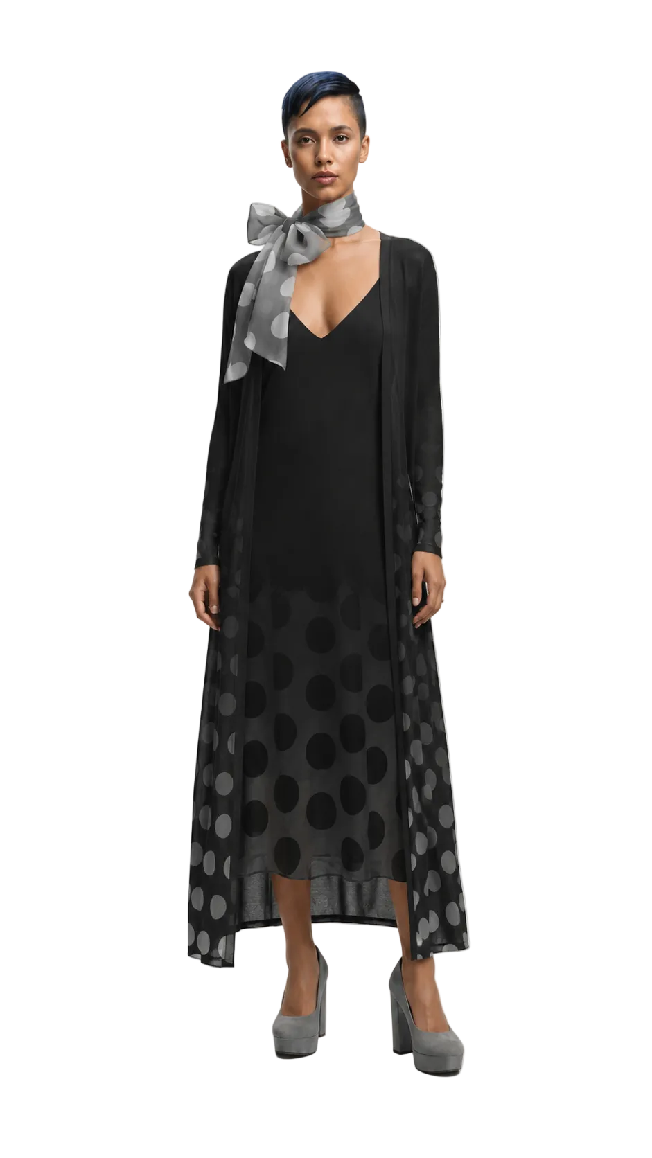 A model wearing a black midi dress with a sheer black polka dot overlay, a black cardigan, a gray patterned neck scarf, and gray high heels, photographed against a light gray studio background.