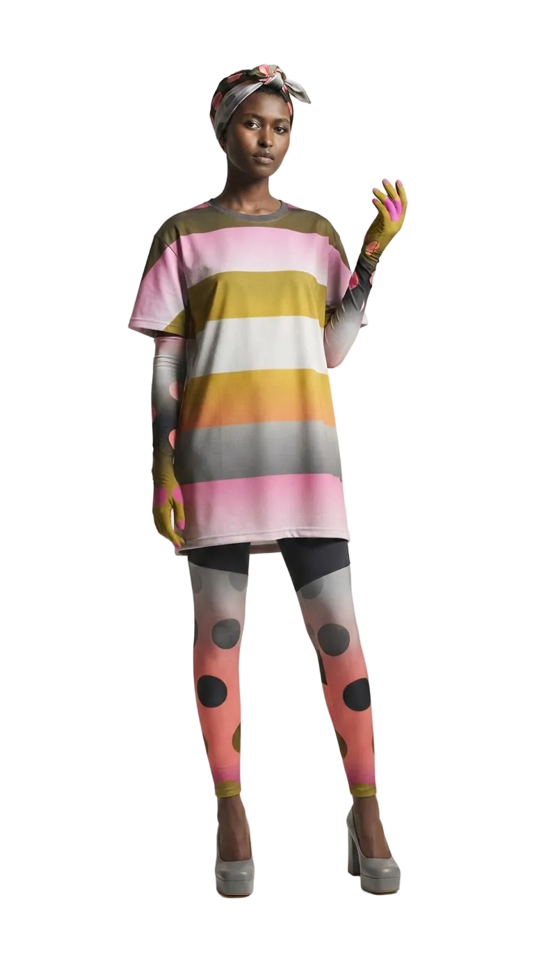 A model wearing a colorful horizontally striped tunic top with pink, yellow, white, and gray stripes, paired with pink polka-dot tights and gray platform heels, against a plain light background.